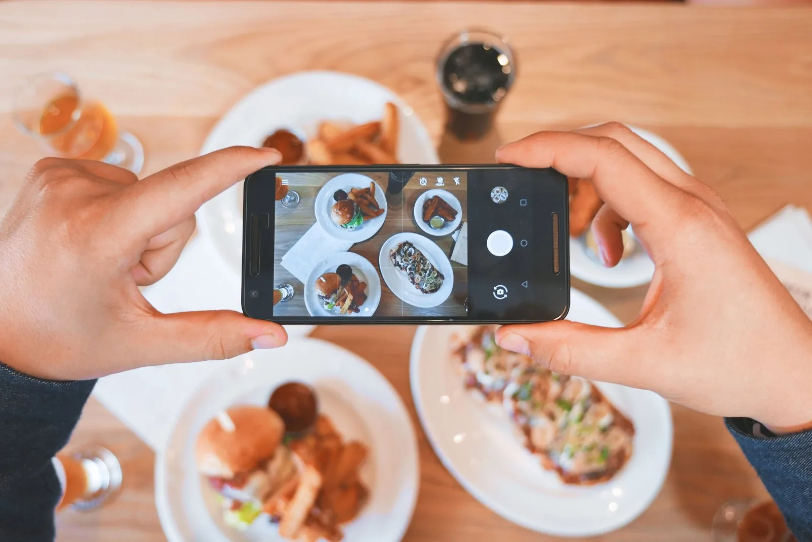 Unas manos fotografían con el móvil varios platos sobre una mesa